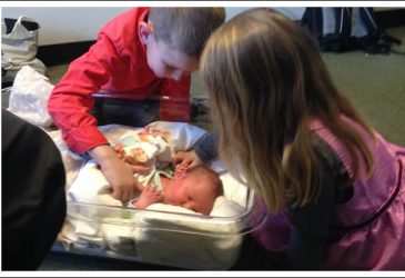 Siblings looking at a newborn baby.