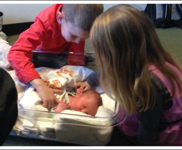 Siblings looking at a newborn baby.