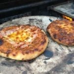 two small pizzas on a pizza stone on an outdoors grill