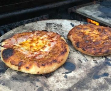 two small pizzas on a pizza stone on an outdoors grill