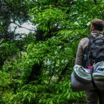 man hiking in the woods with a backpack with a rolled up sleeping bag