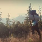 man hiking with sleeping pad and backpack in mountaines landscape