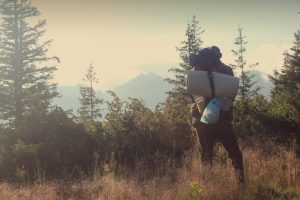 man hiking with sleeping pad and backpack in mountaines landscape